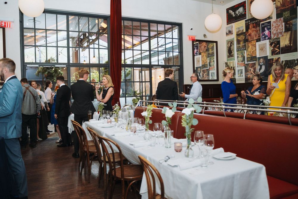 Elegant wedding reception dinner setup in a stylish restaurant with large windows and red booths.