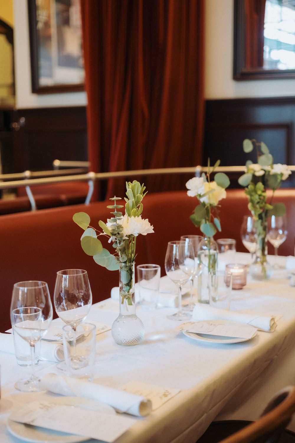 Elegant wedding reception table set with white linens, glass vases of eucalyptus and white flowers, and crystal stemware.