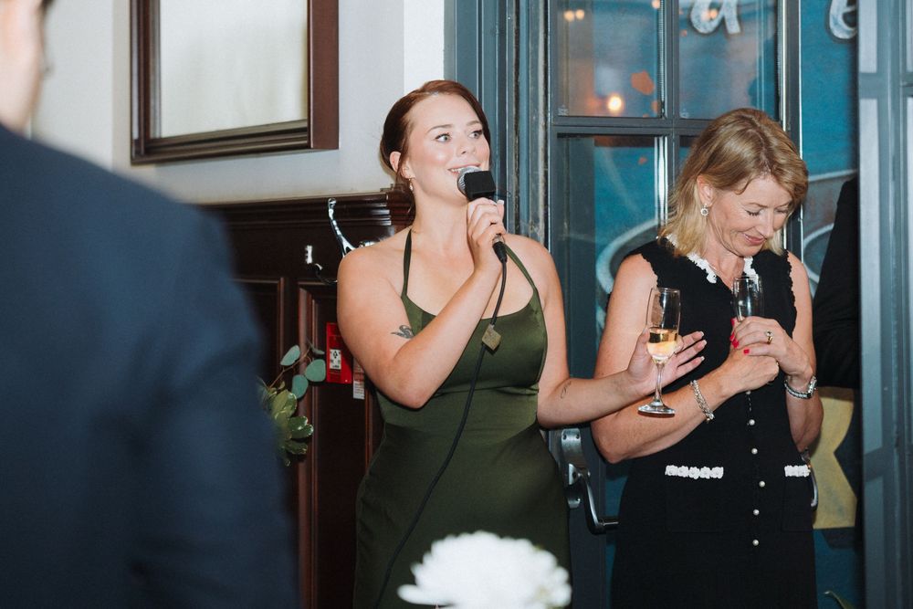 Woman in an olive green dress gives a heartfelt speech with a microphone at a wedding reception.