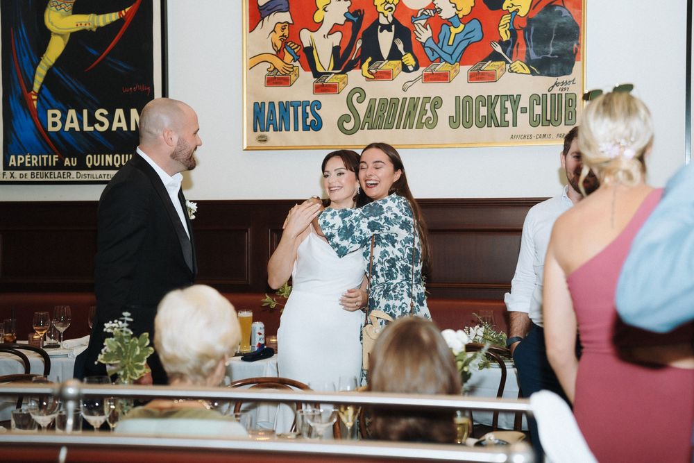 Bride and female guest share a warm hug while giving a speech at an elegant restaurant wedding reception.