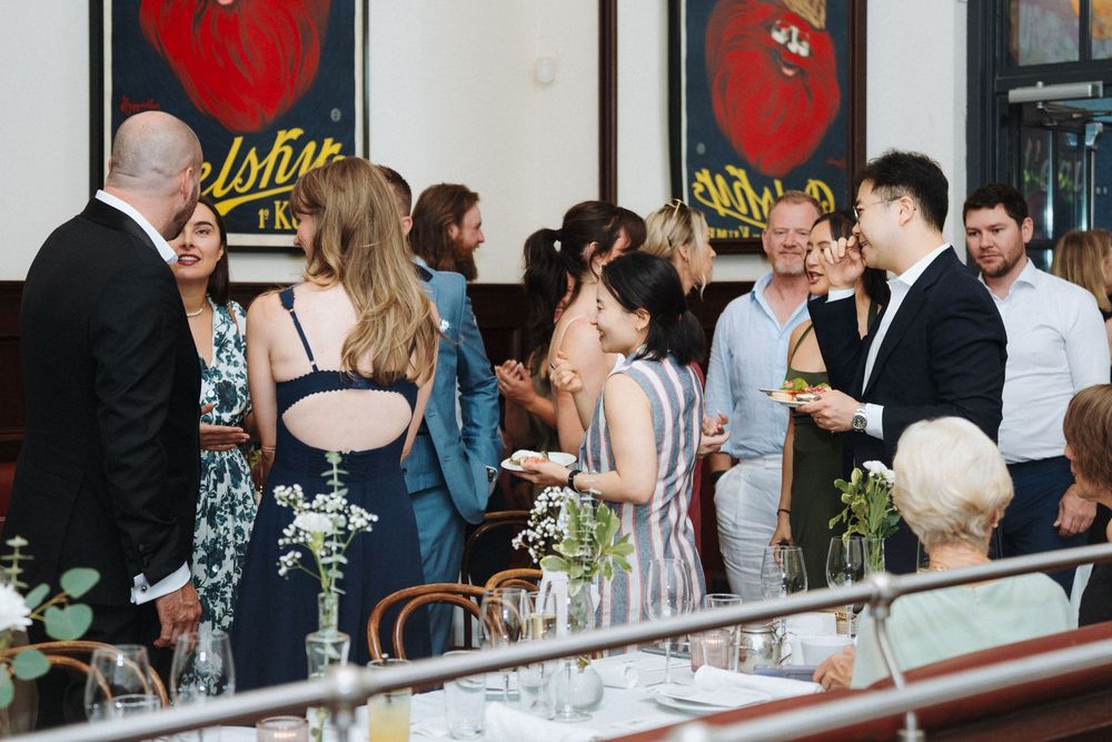 Wedding guests mingle and socialize at a stylish reception venue with floral centerpieces on tables.