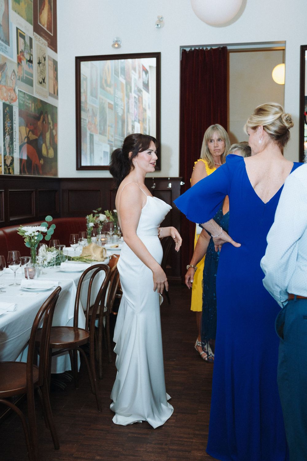 Bride in white gown smiles warmly as a guest in blue dress greets her at wedding reception venue.