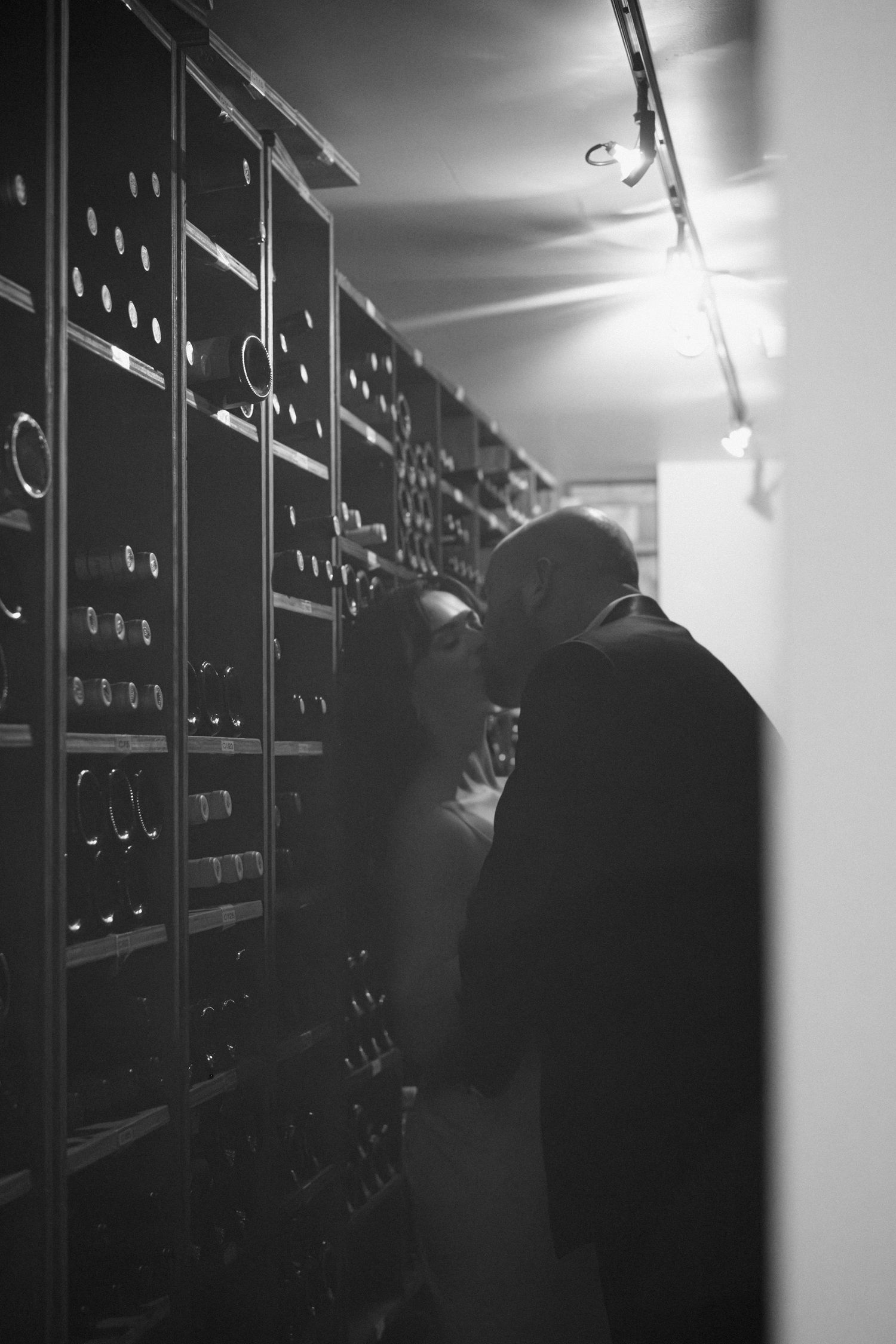 Black and white photo of a couple sharing a romantic moment in a dimly lit wine cellar corridor.