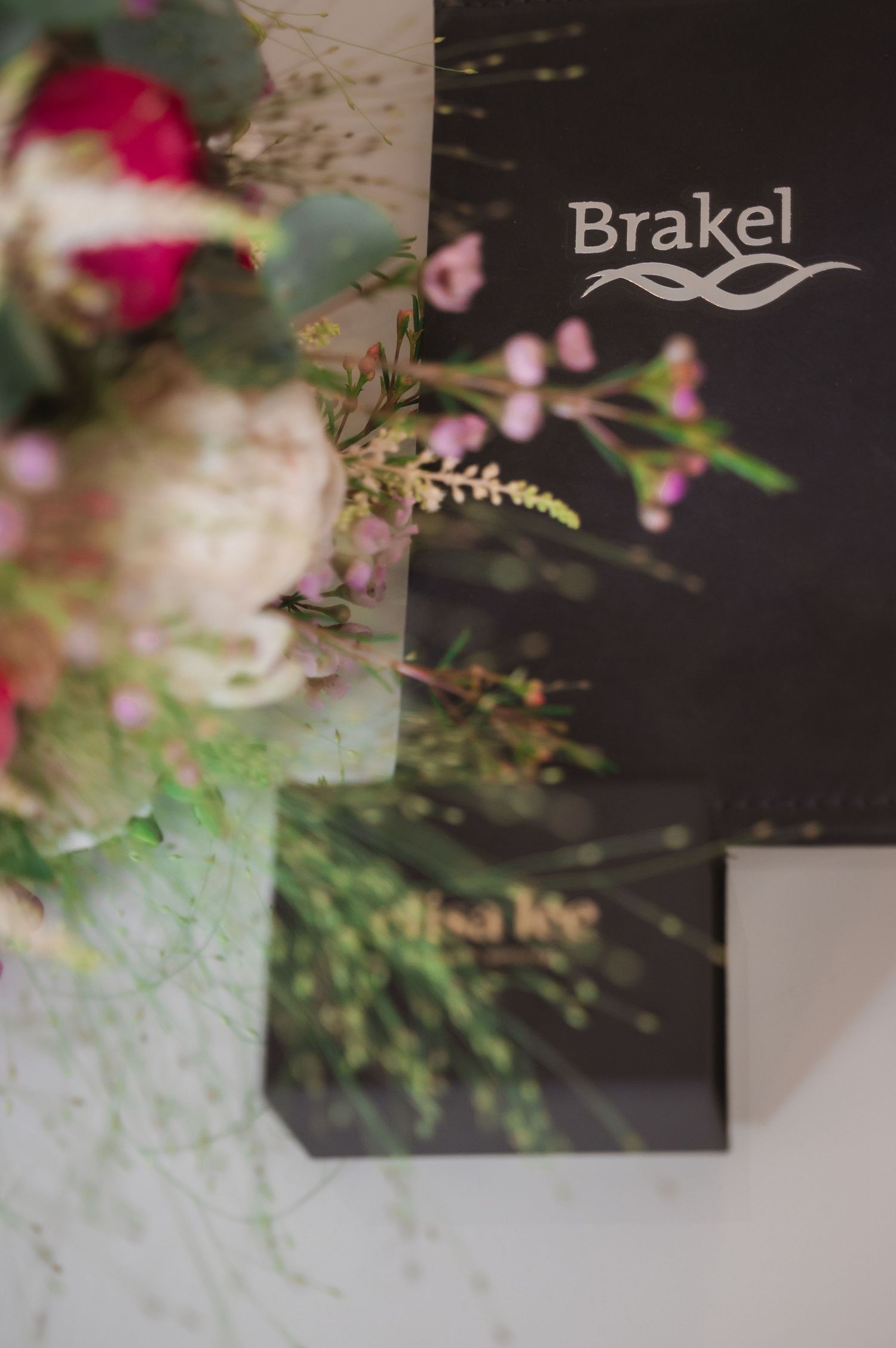 Brakel branded black folder beside a colorful floral bouquet with pink roses and greenery on a white surface.