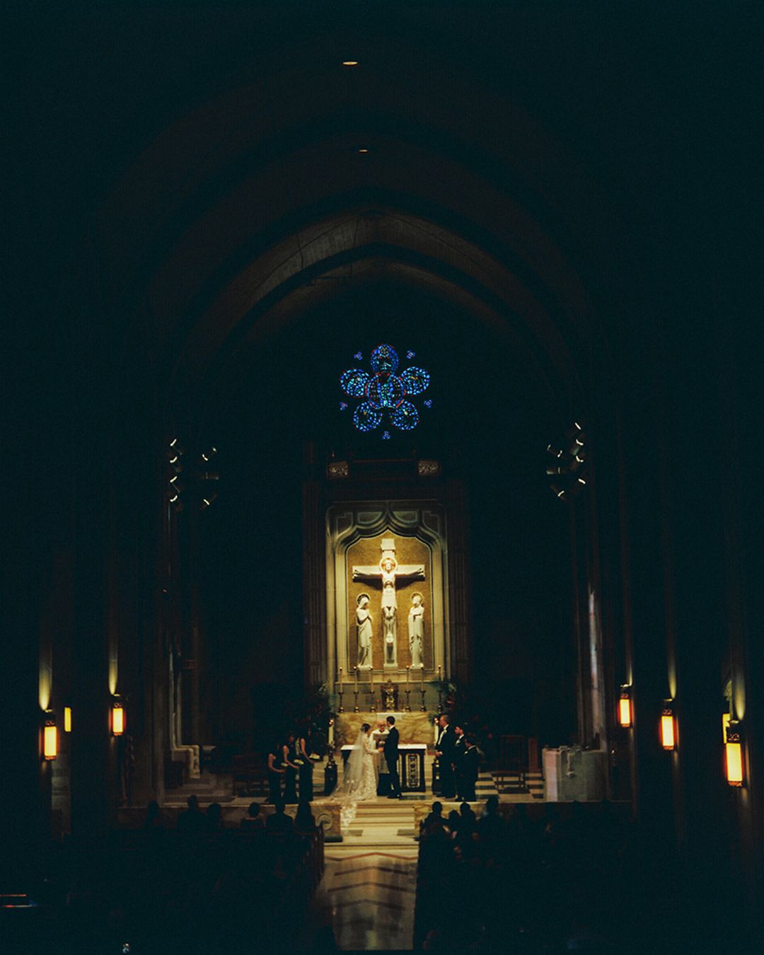 Dark church interior illuminated by candlelight with an ornate altar and arched architecture visible in the distance.