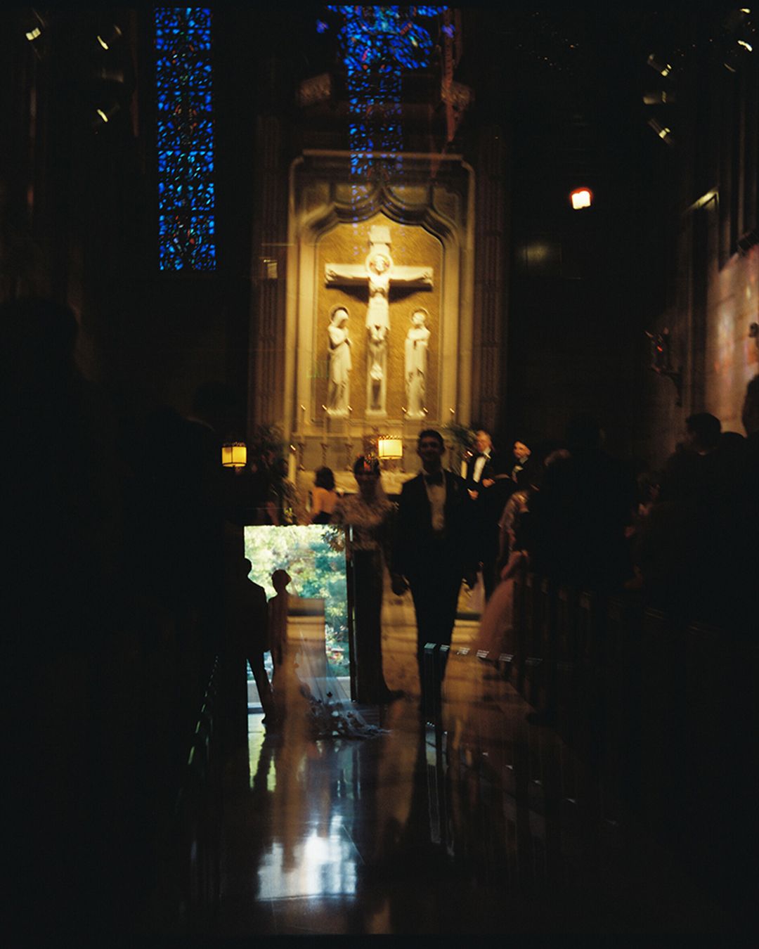 Dimly lit church sanctuary with blue stained glass windows and golden altar illuminated in the background.