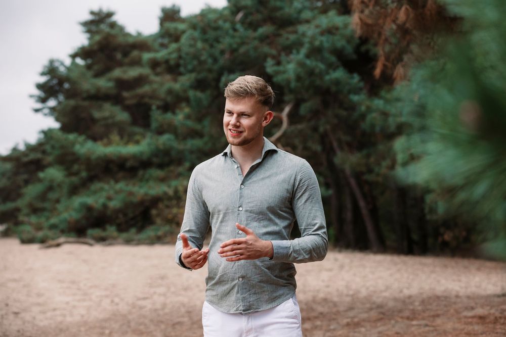 Candid shot of someone in gray button-down and white pants walking through a wooded area.