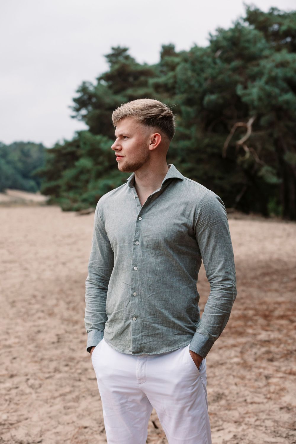 Side profile portrait of person in gray shirt and white pants with forest scenery behind.