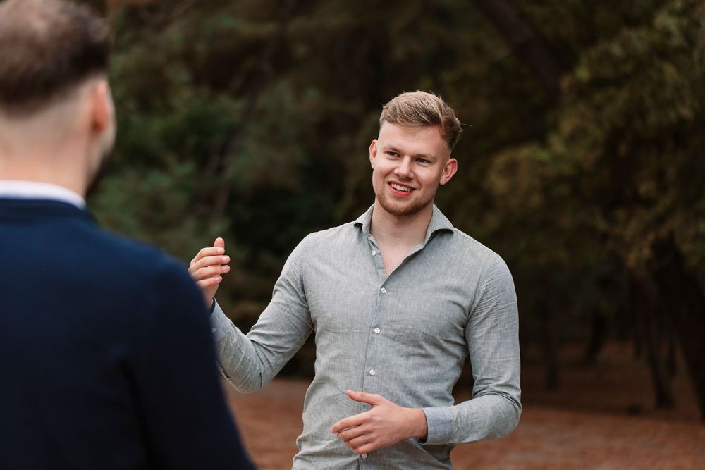 Person wearing grey collared shirt engaged in expressive conversation outdoors.