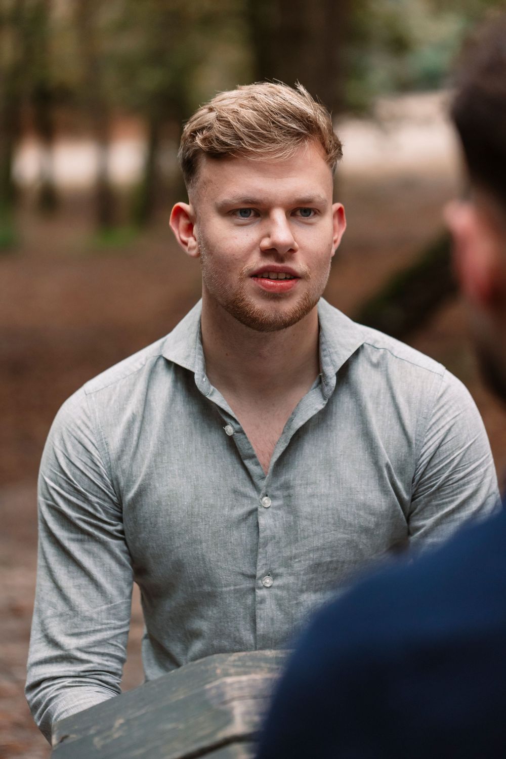 Individual in grey shirt having an intense discussion outdoors among trees.