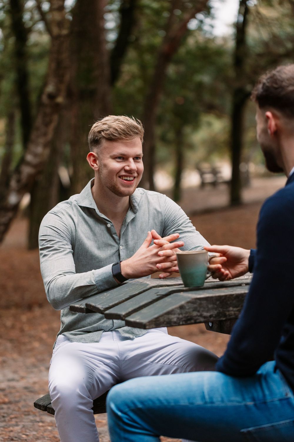 Two people sharing conversation over coffee at rustic outdoor table.