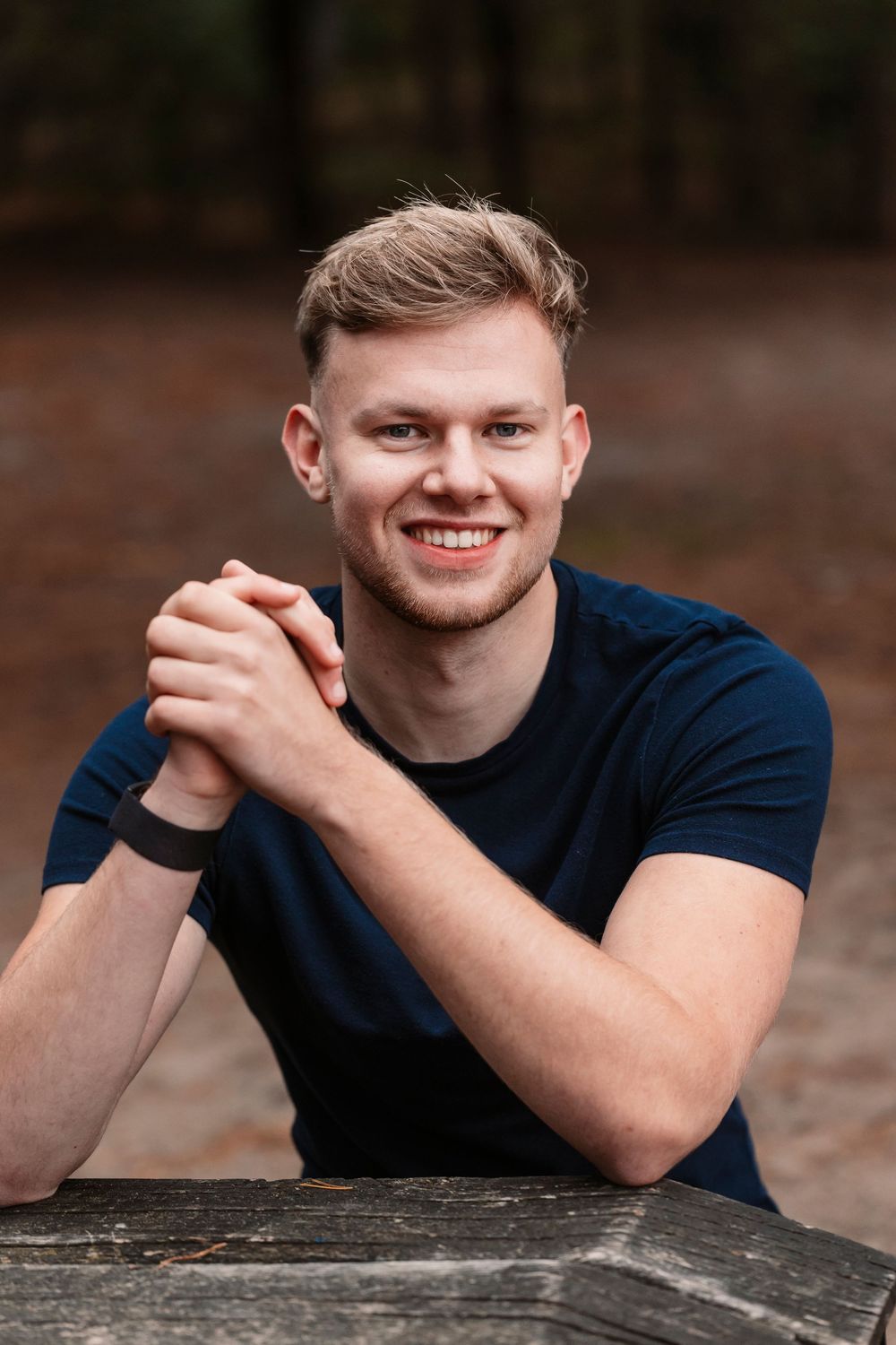 Person in navy shirt leaning on wooden surface outdoors with friendly expression.
