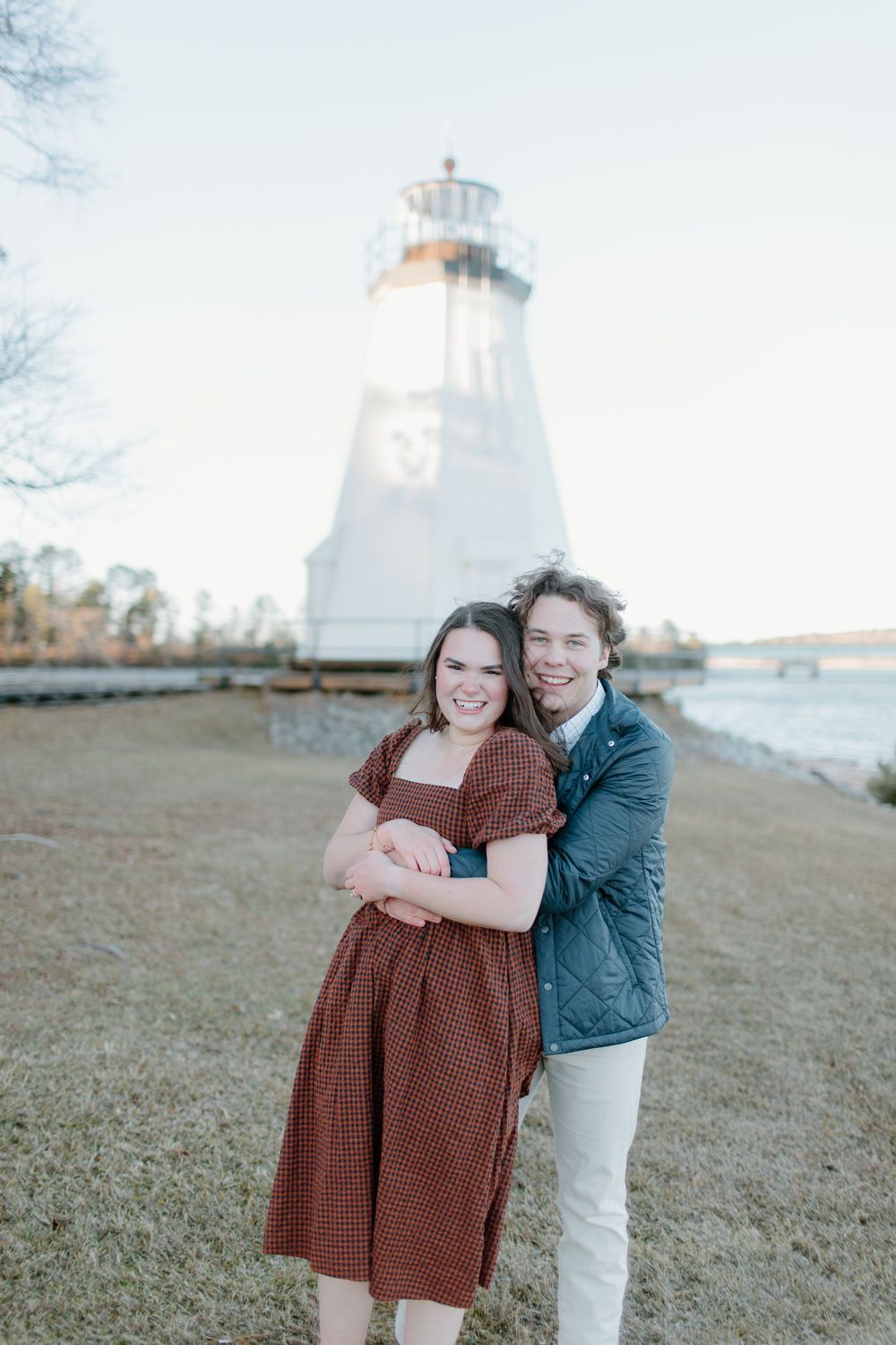 Engagement photos with lighthouse backdrop showing couple in casual winter outfits.