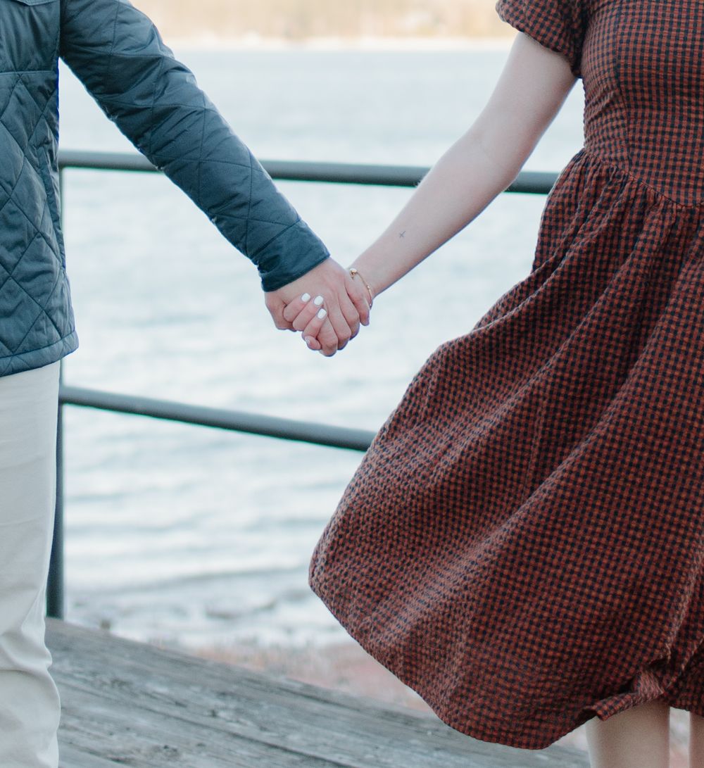 Detail shots of couple holding hands while walking along waterfront railing.