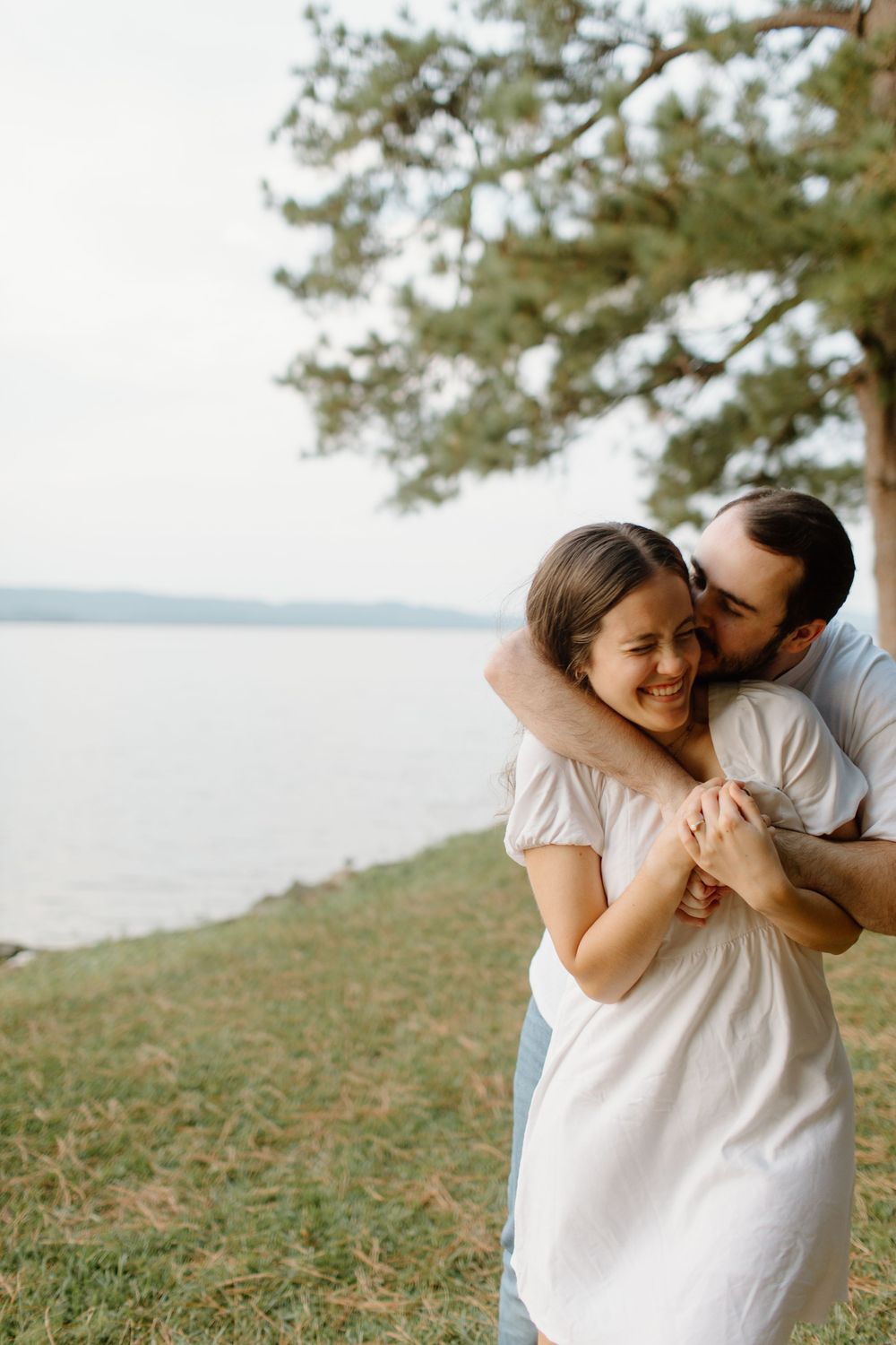 Couple sharing tender moments on a grassy hillside overlooking a lake.