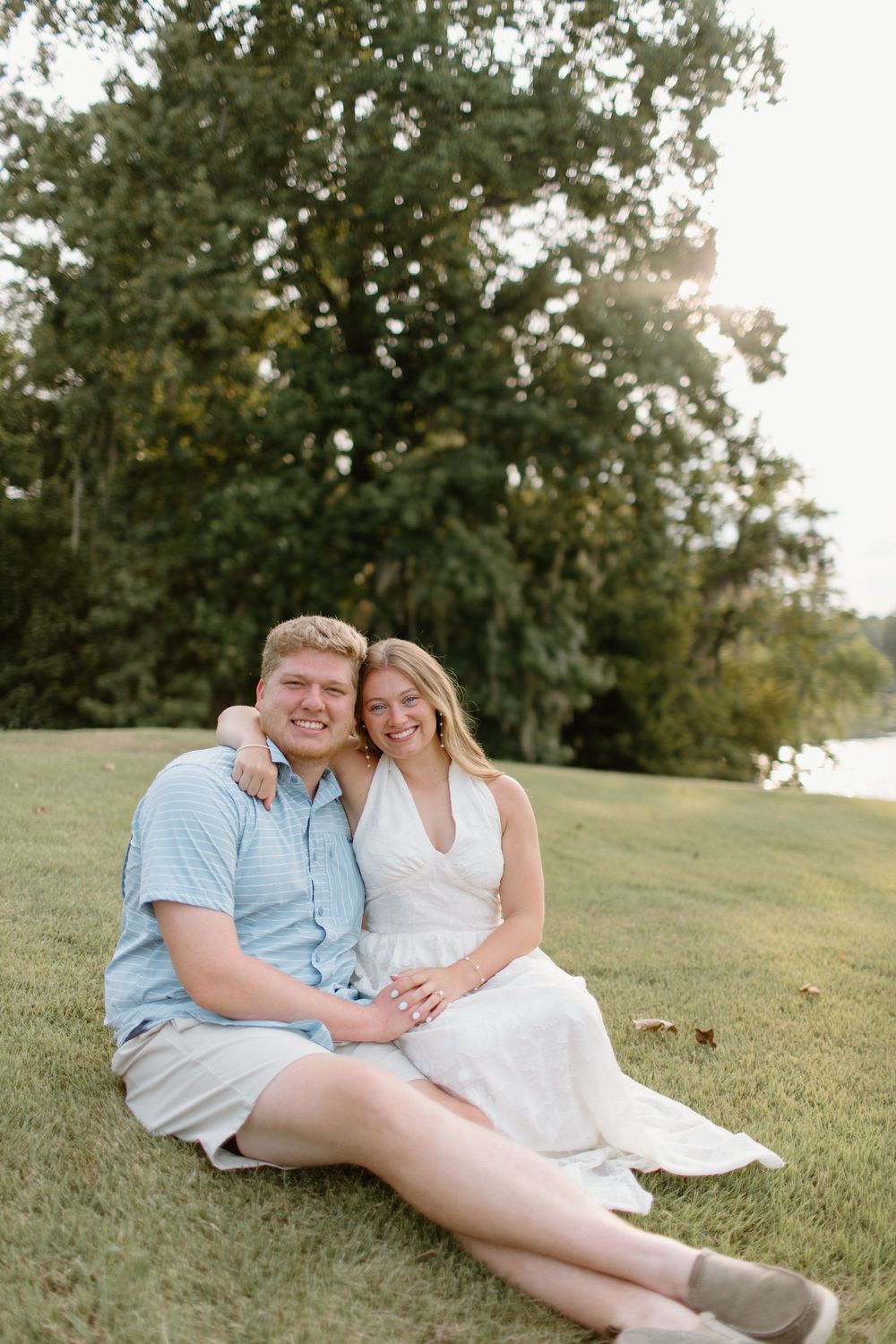 Couple relaxing on grassy hill during outdoor photo session.