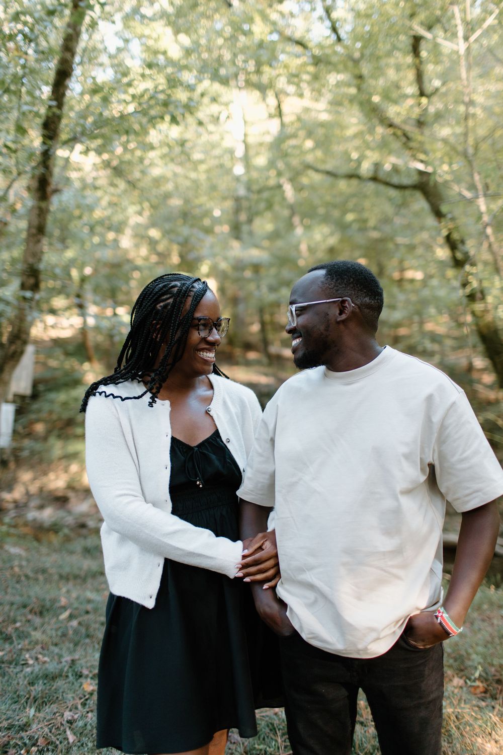 Couple sharing intimate moments in a wooded outdoor setting wearing black and white outfits.