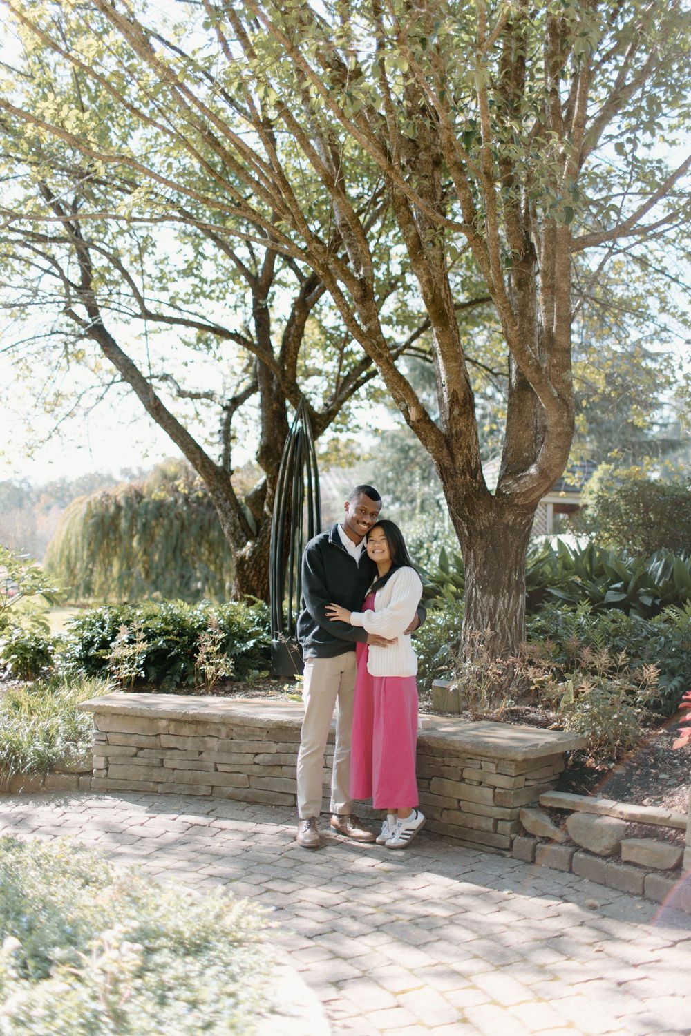 Couple enjoying intimate moments along stone wall pathway in natural setting.