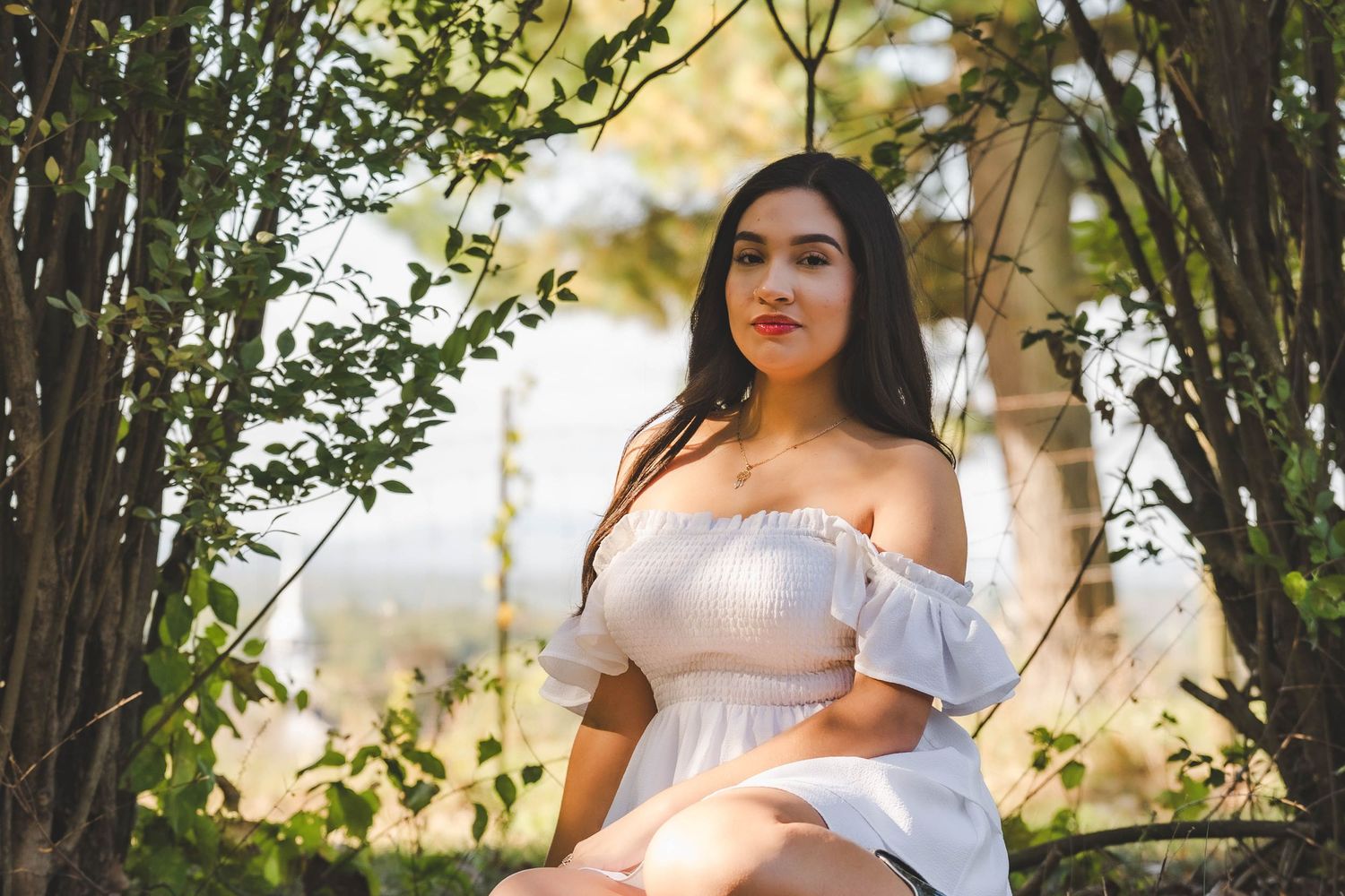 A white off-shoulder dress photoshoot in a natural outdoor setting with trees.