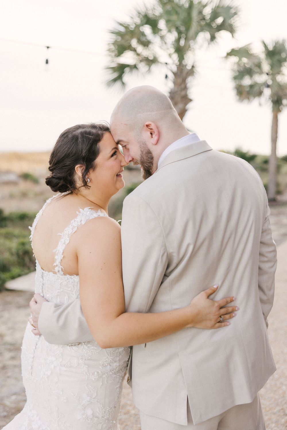 A couple in wedding attire embraces on a beach with palm trees in the background, shown in multiple candid shots.