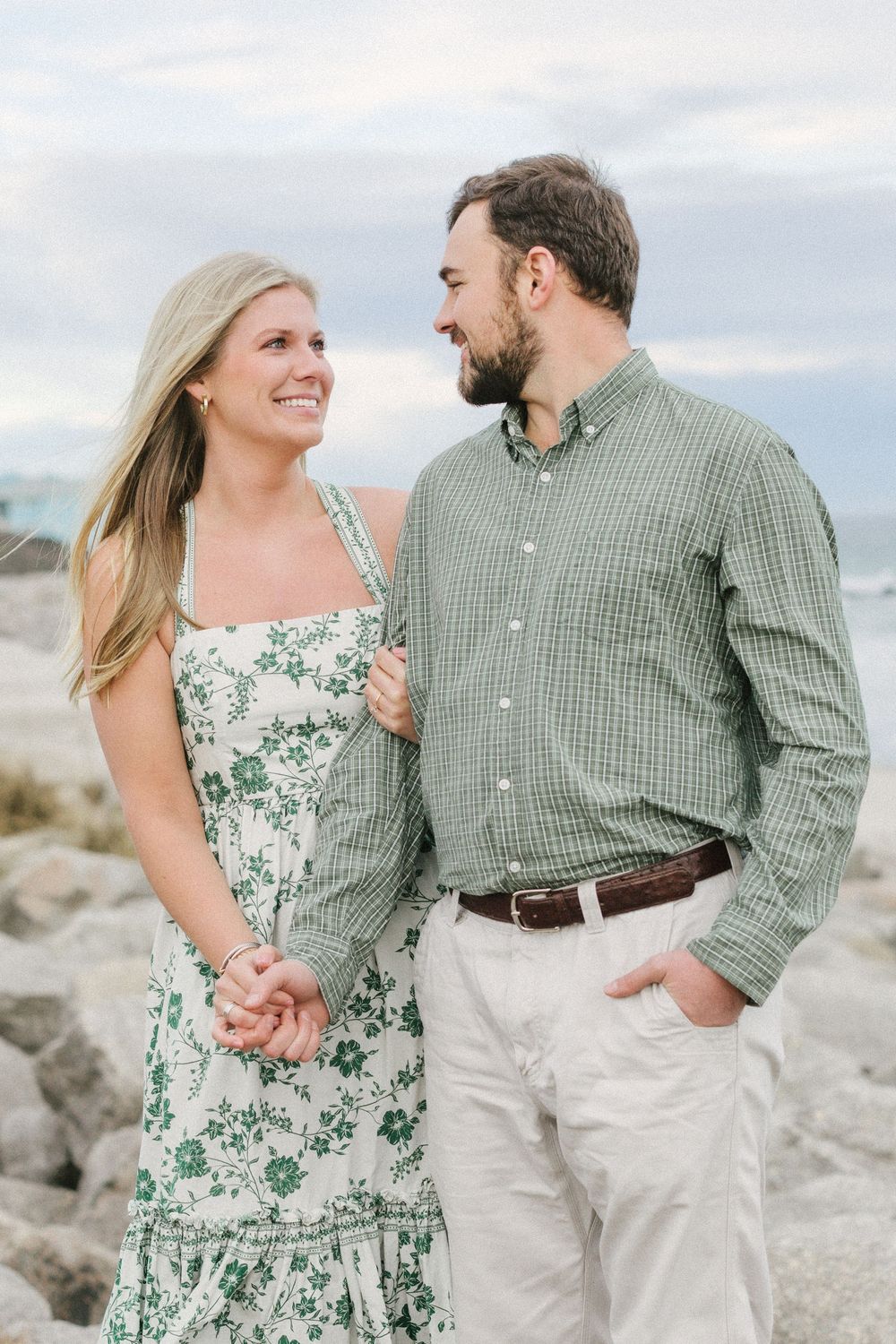A couple in coordinating green outfits shares romantic moments on a rocky beach during a photo session.