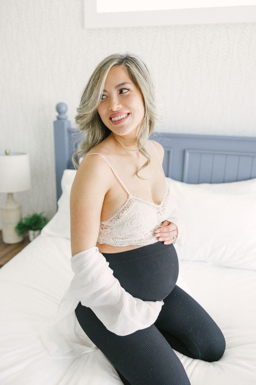 Person in casual black and white outfit poses on white bedding in bright bedroom setting.