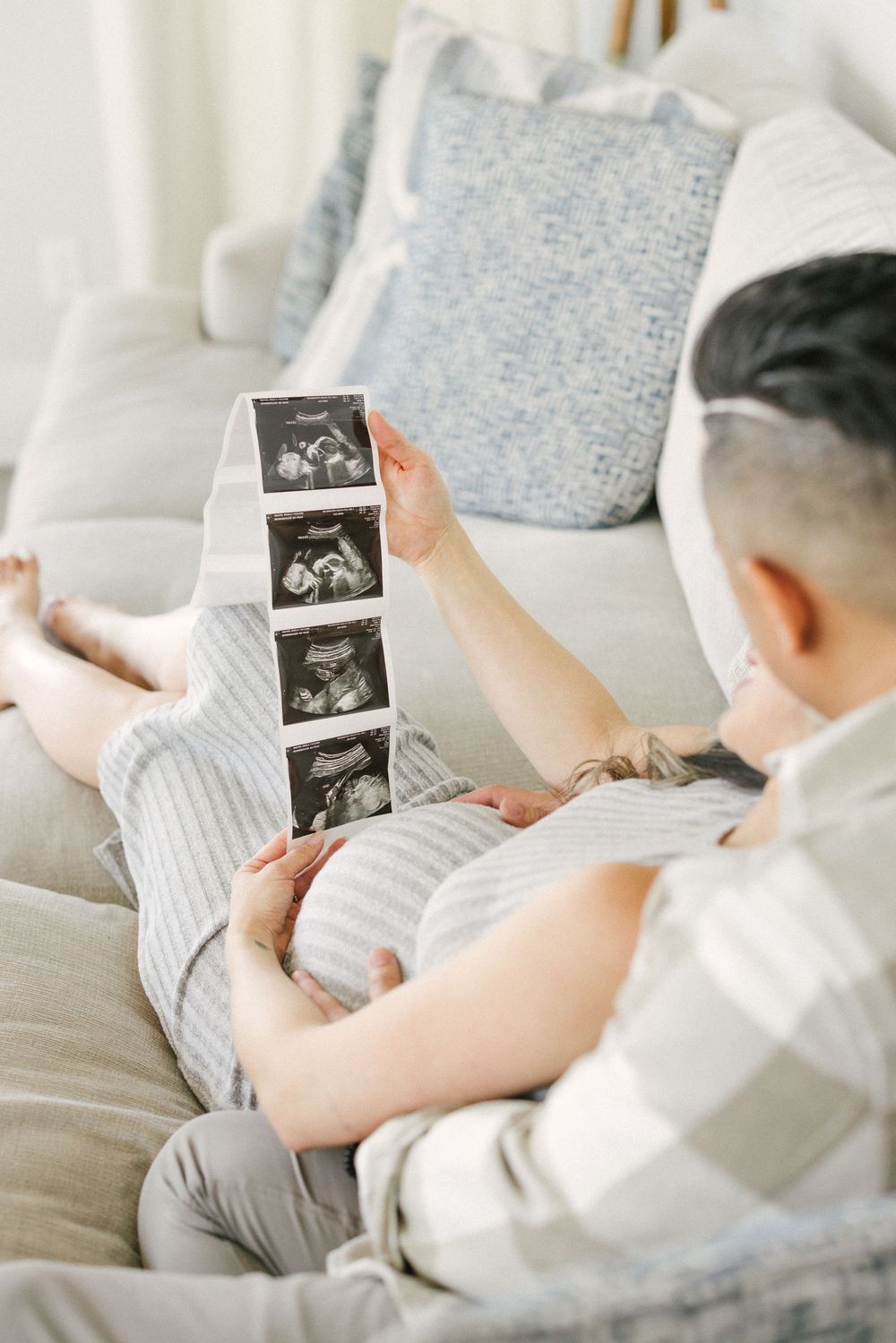A series of ultrasound photos being held and viewed while sitting on a cozy gray couch.