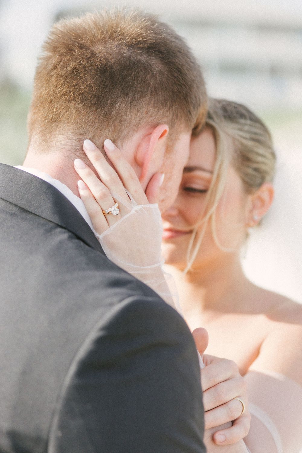 Intimate wedding moment captured in soft light as couple shares tender embrace with bride's hand showing engagement ring.