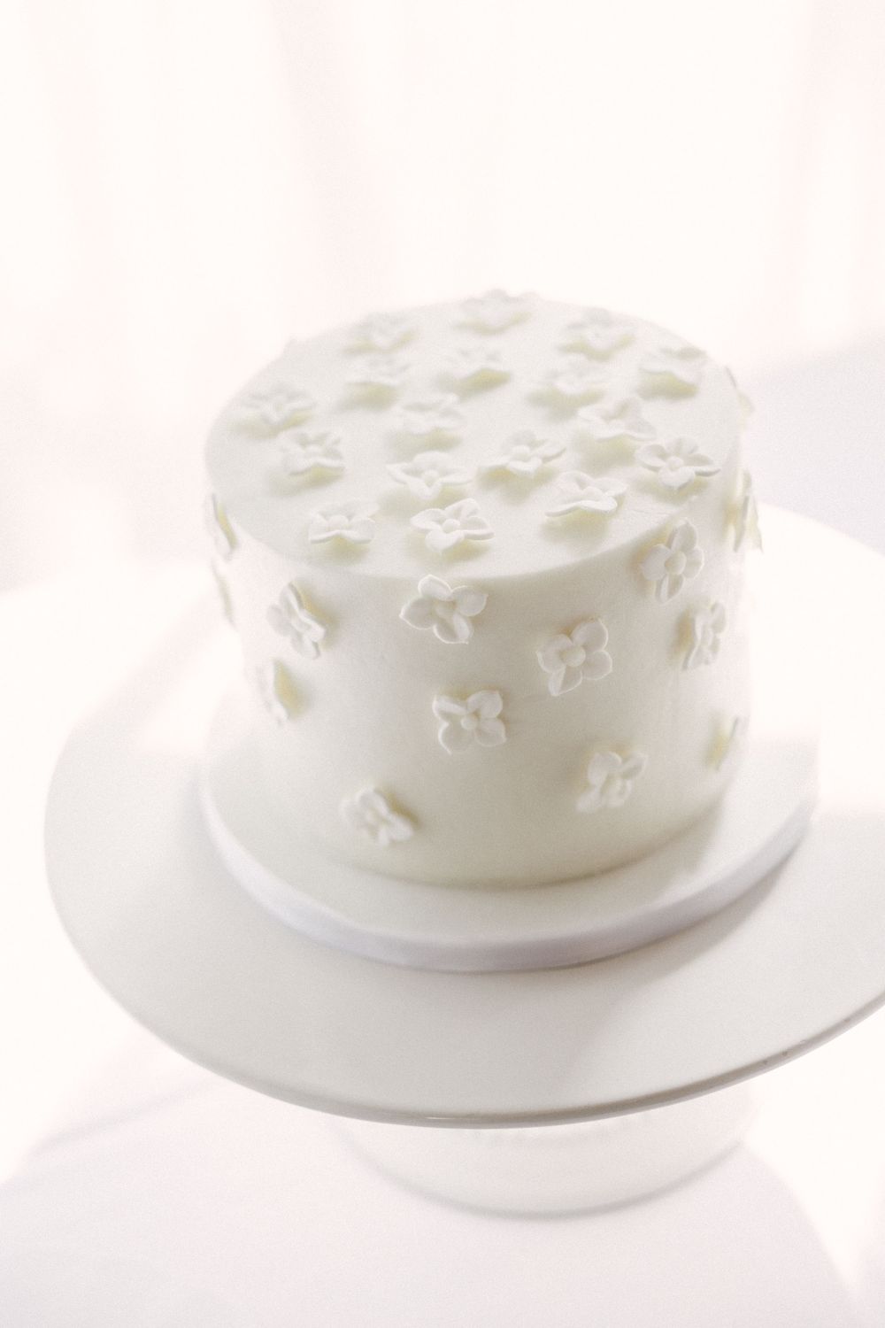 White fondant covered cake decorated with delicate floral patterns shown from multiple angles on white plates.