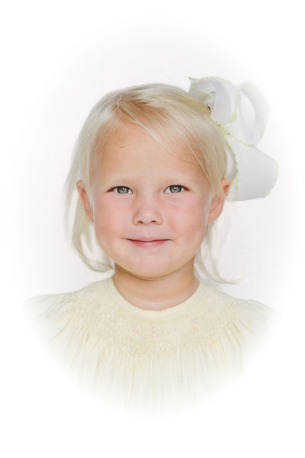 Portrait of a young child with light blonde hair wearing a white bow and cream colored top against a white background.