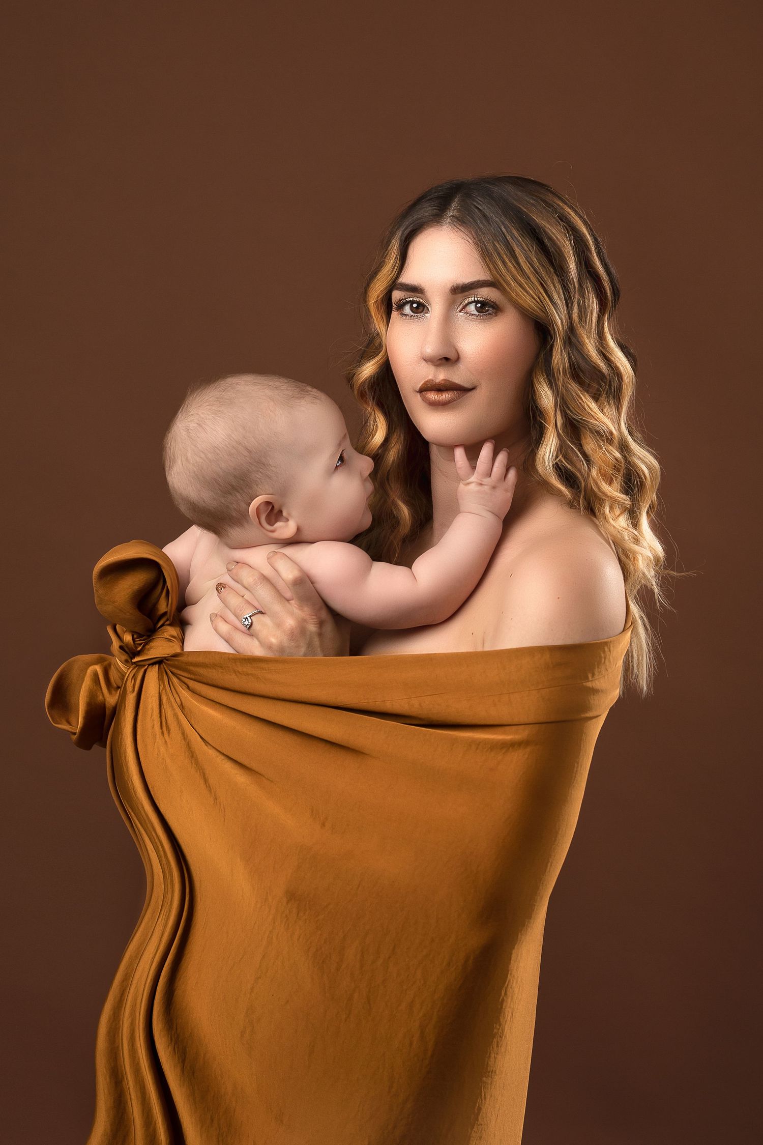 A series of intimate artistic portraits showing a tender nursing moment between parent and baby against a brown backdrop.
