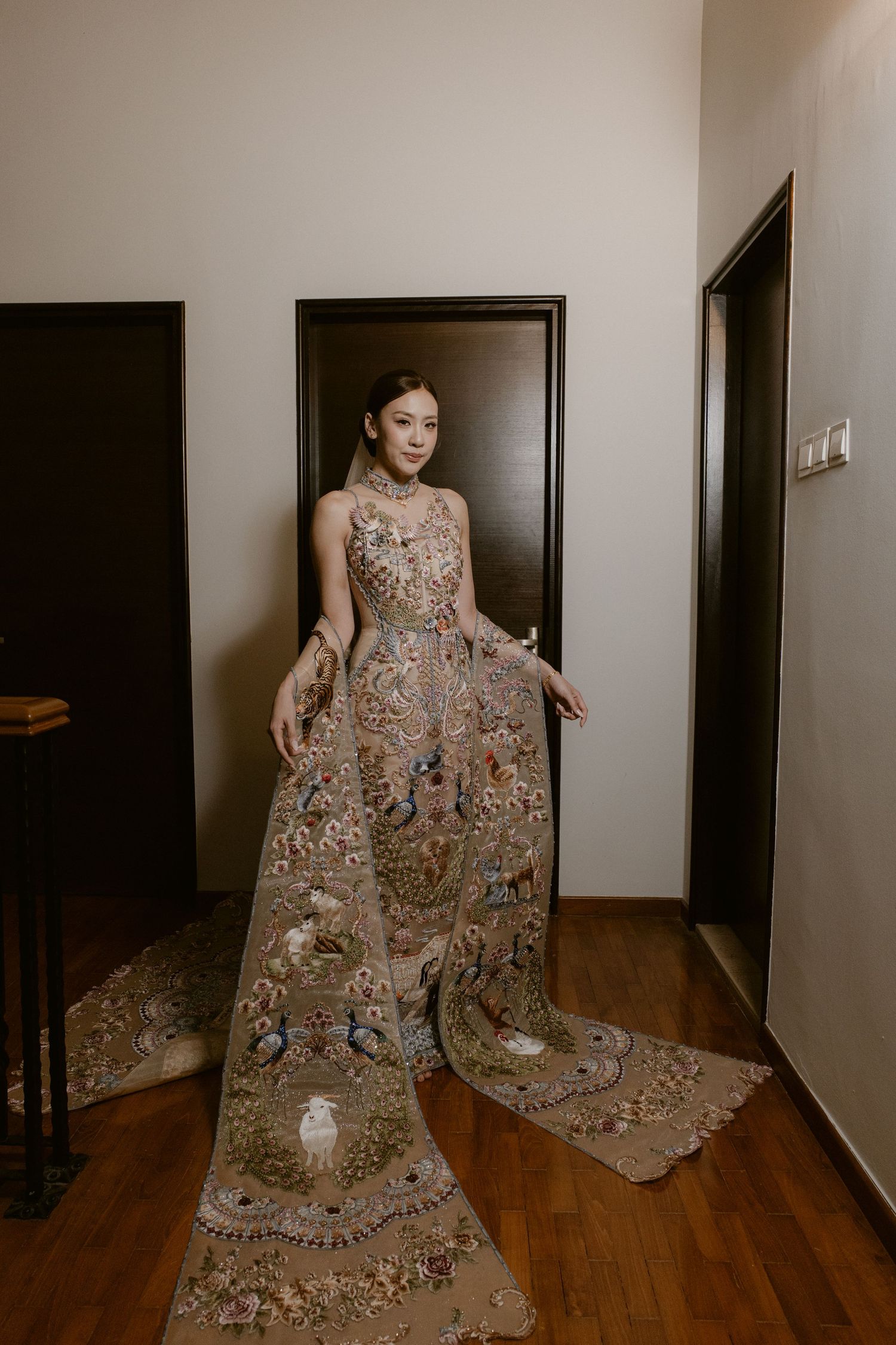Bride in an elaborate floral embroidered gown with long train standing in a hallway.