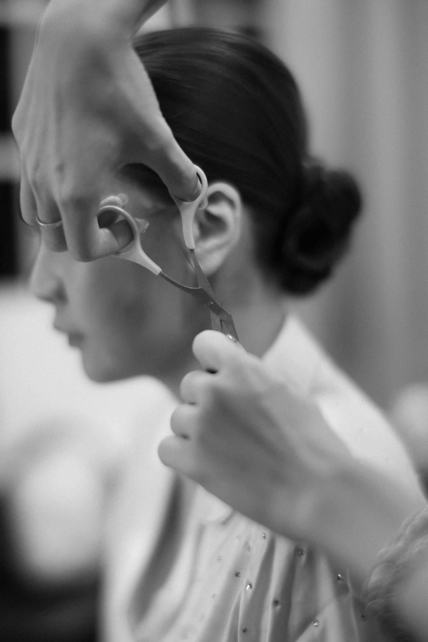 Black and white photo of hairstylist trimming bride's hair with scissors during wedding preparation.