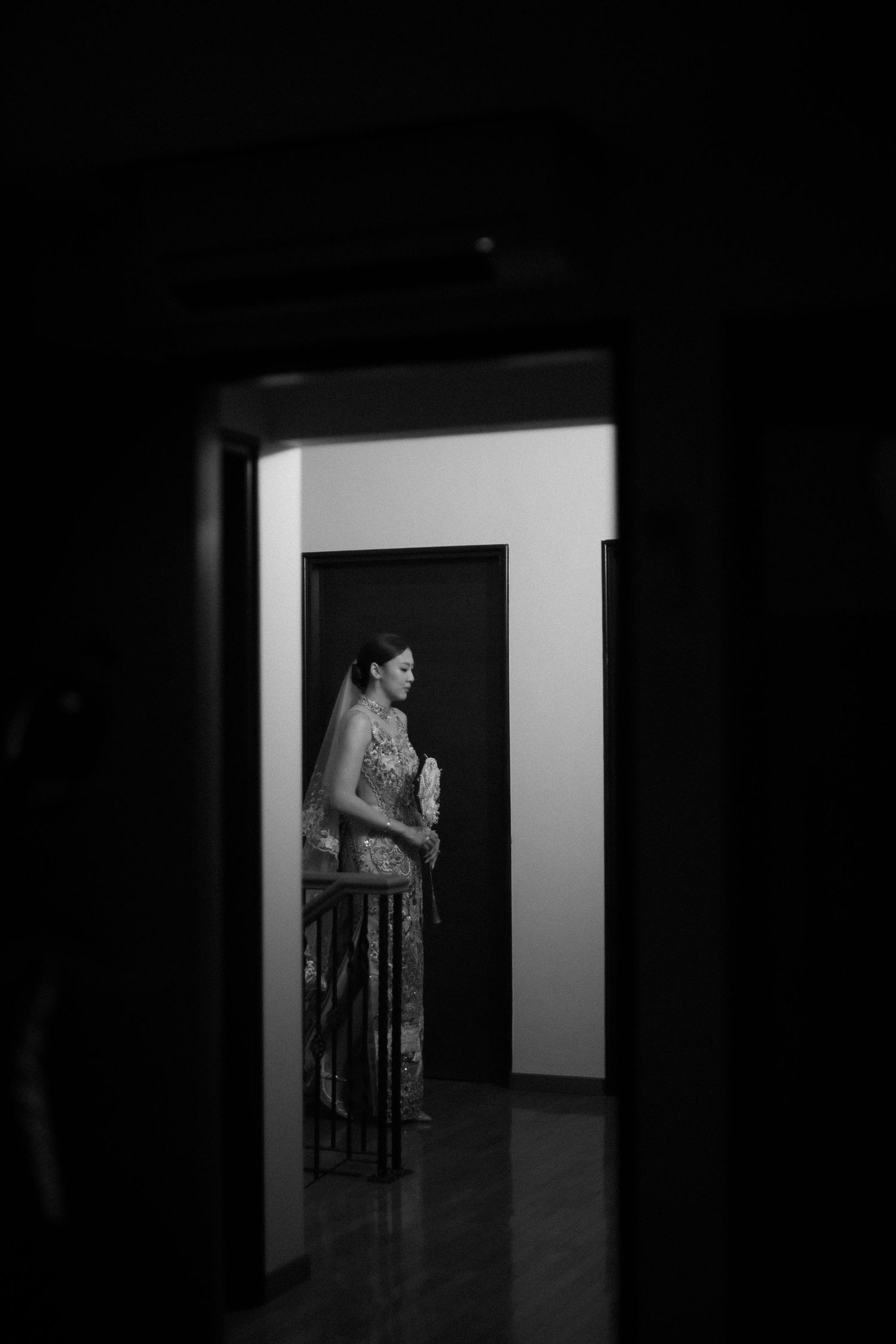 Black and white artistic shot of bride in embellished gown framed in doorway during wedding preparations.