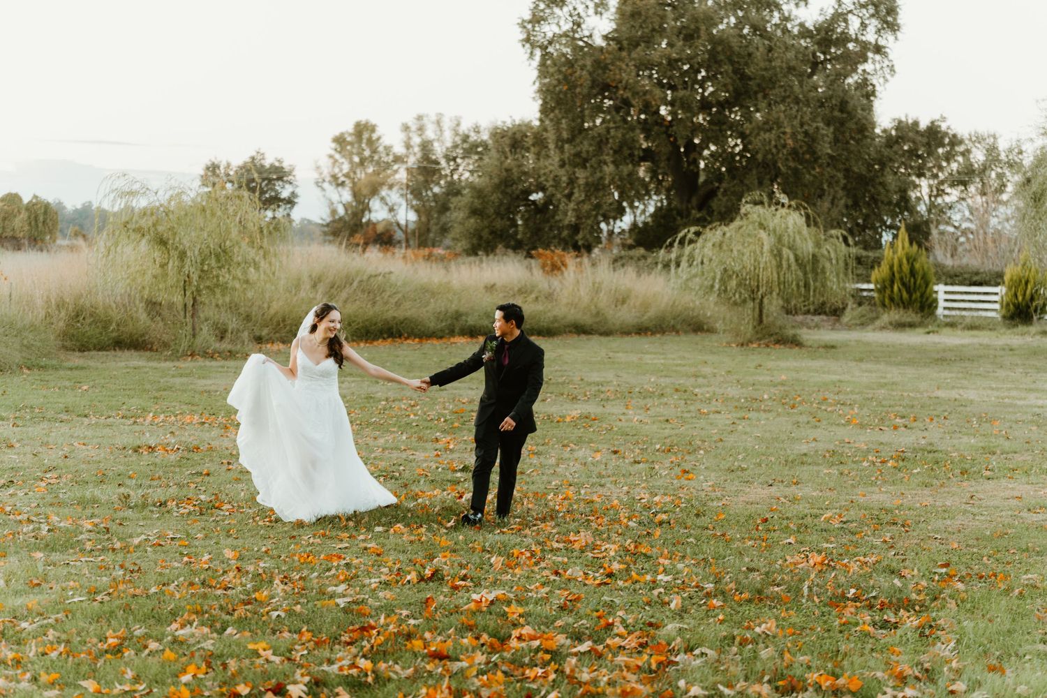 Bride and groom dance together in autumn field scattered with colorful fallen leaves.