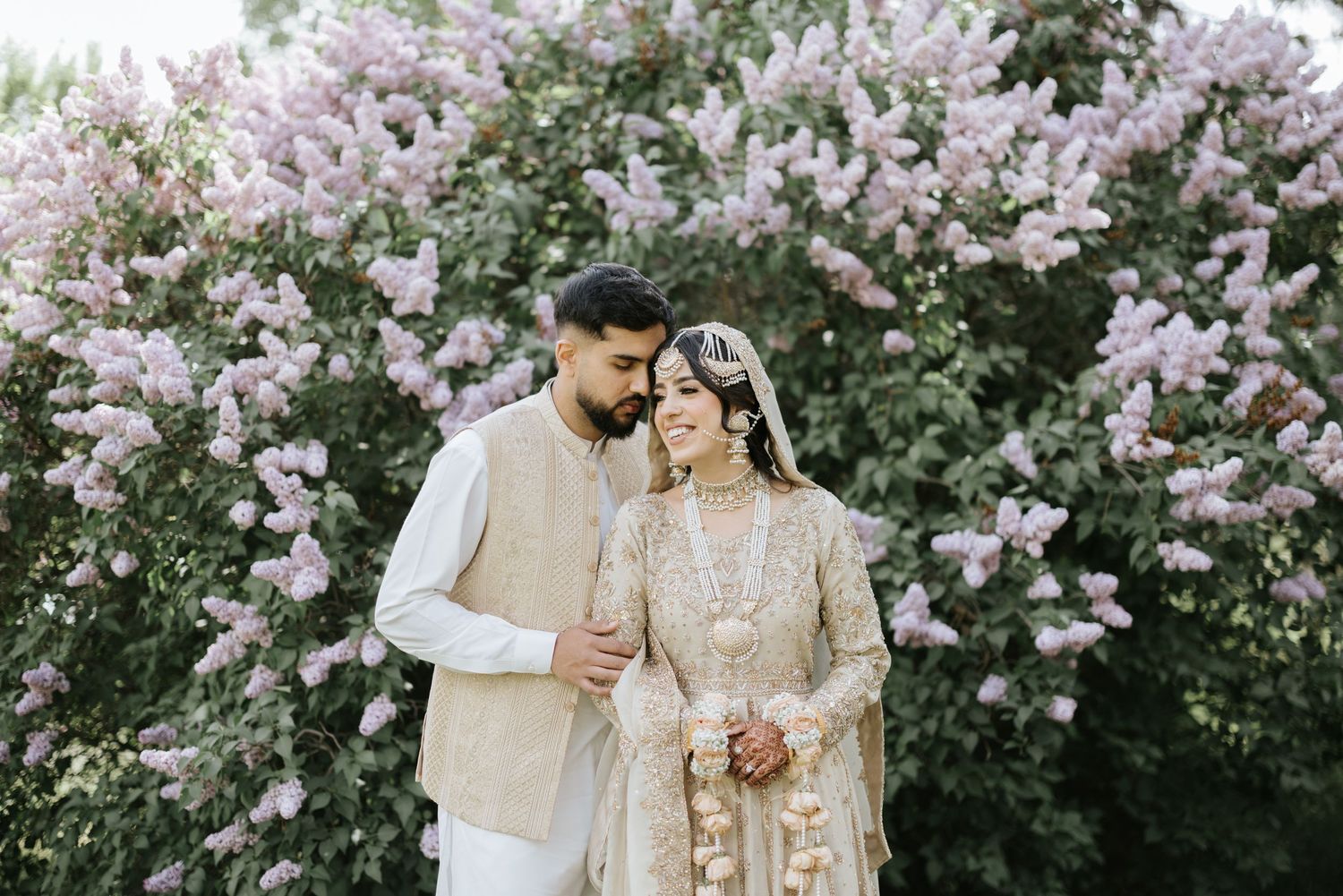 A bride in red surrounded by bridesmaids wearing neutral tones on a manicured lawn.