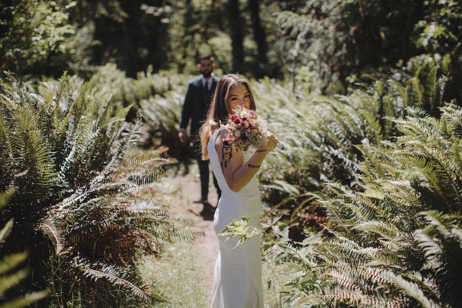 A couple poses for wedding photos against a dramatic mountain backdrop with evergreen trees and a scenic lake.