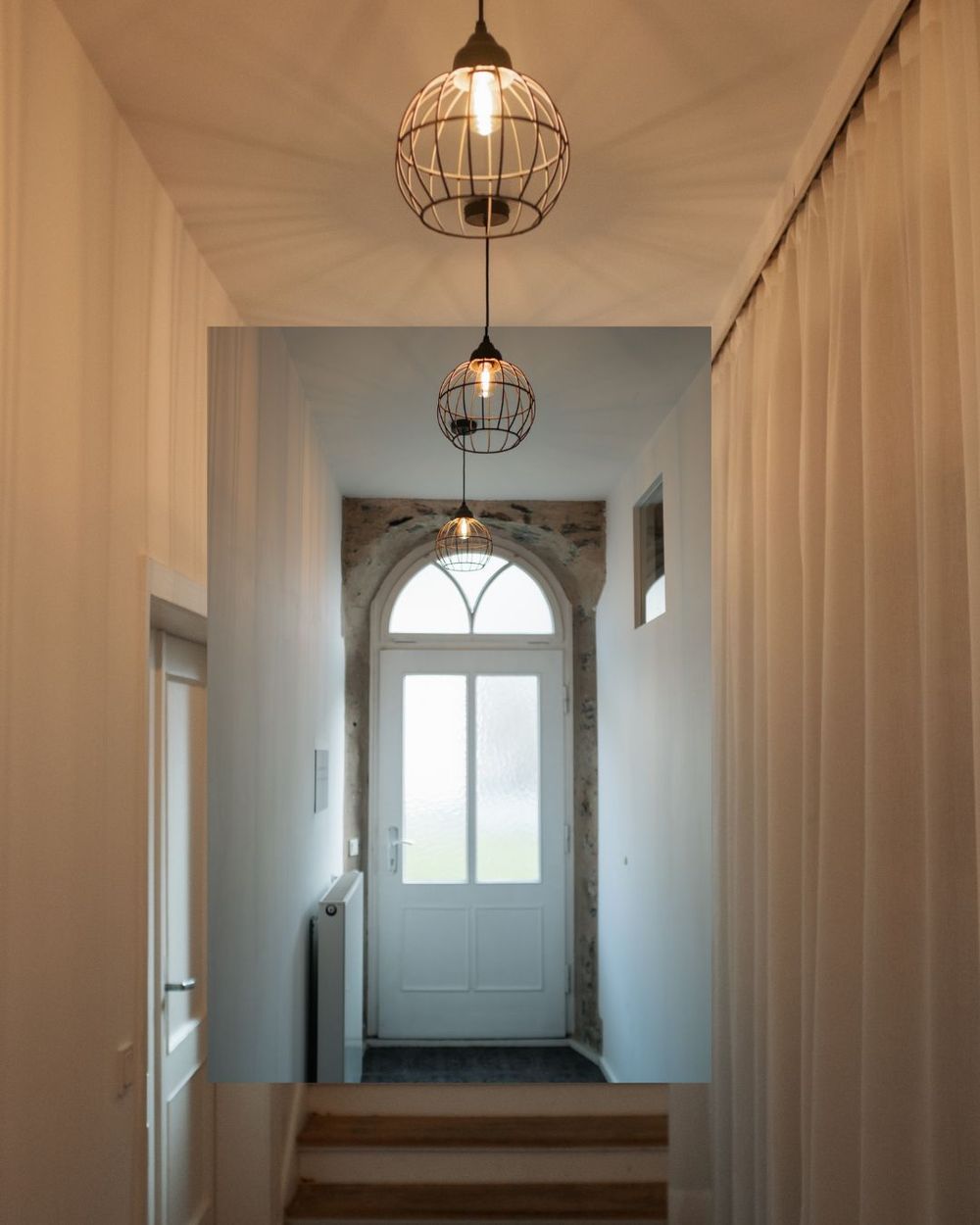 Elegant hallway with pendant cage lights and white curtains leading to an arched window entrance.