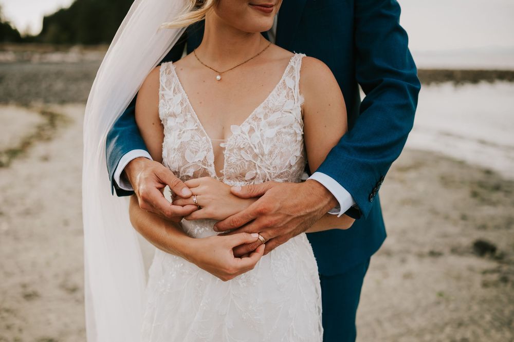 Wedding photography of couple on Williams Beach close up of hands and rings during golden hour with ocean, and sand in background