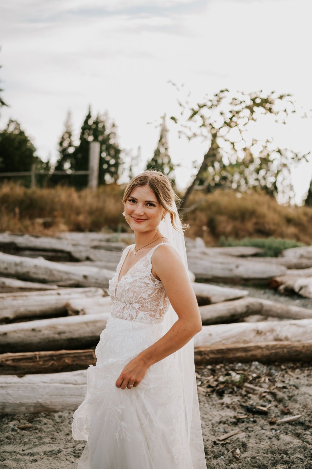 Bride smiling at camera with driftwood and golden grass in the background, wedding photography of couple on Williams Beach
