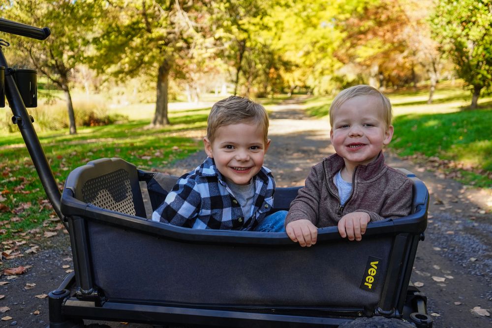 Two children enjoying a wagon ride through a sunny autumn park with golden foliage.