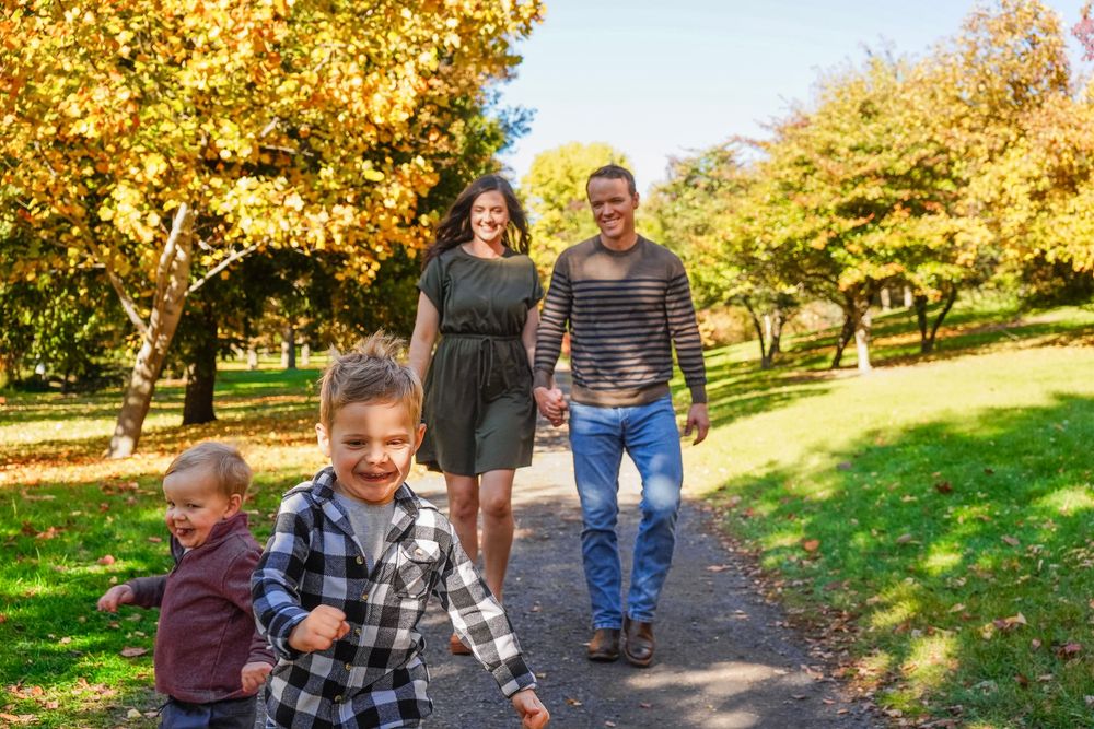 Family walking on a park path surrounded by colorful autumn trees on a sunny day.