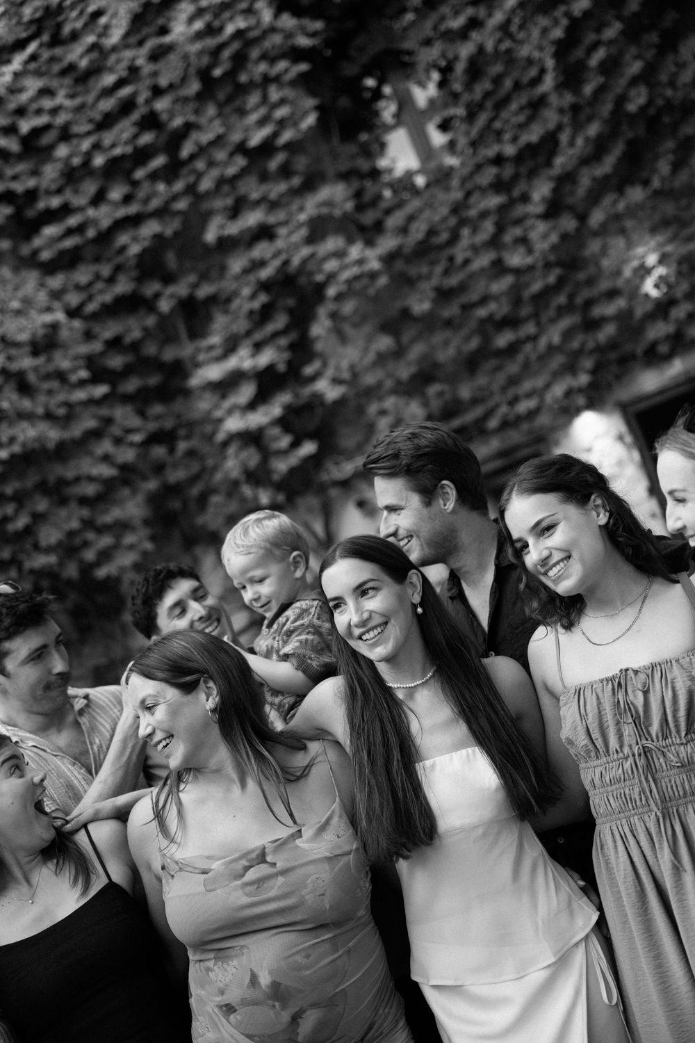 Black and white photo of a joyful group of friends posing together outdoors against an ivy-covered wall.