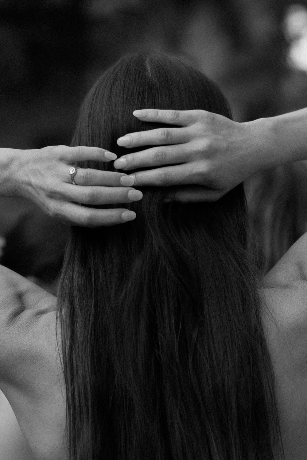 Close-up black and white photo of hands styling long straight hair from behind.