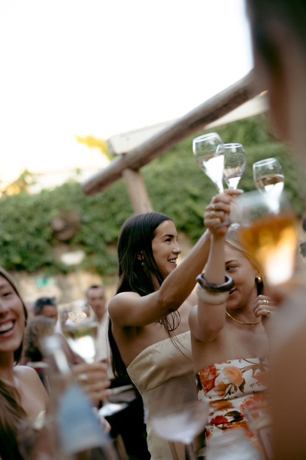 Joyful guests raising champagne glasses in a toast at an outdoor garden celebration during golden hour.