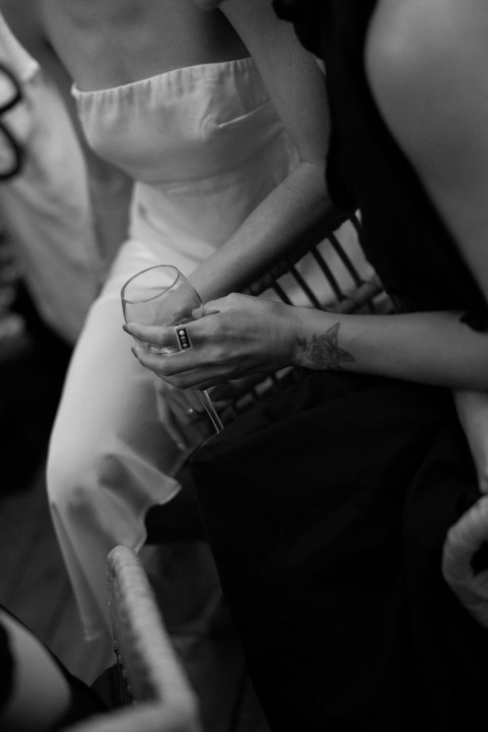 Black and white photo of a bride in a strapless gown holding a glass at a wedding reception.