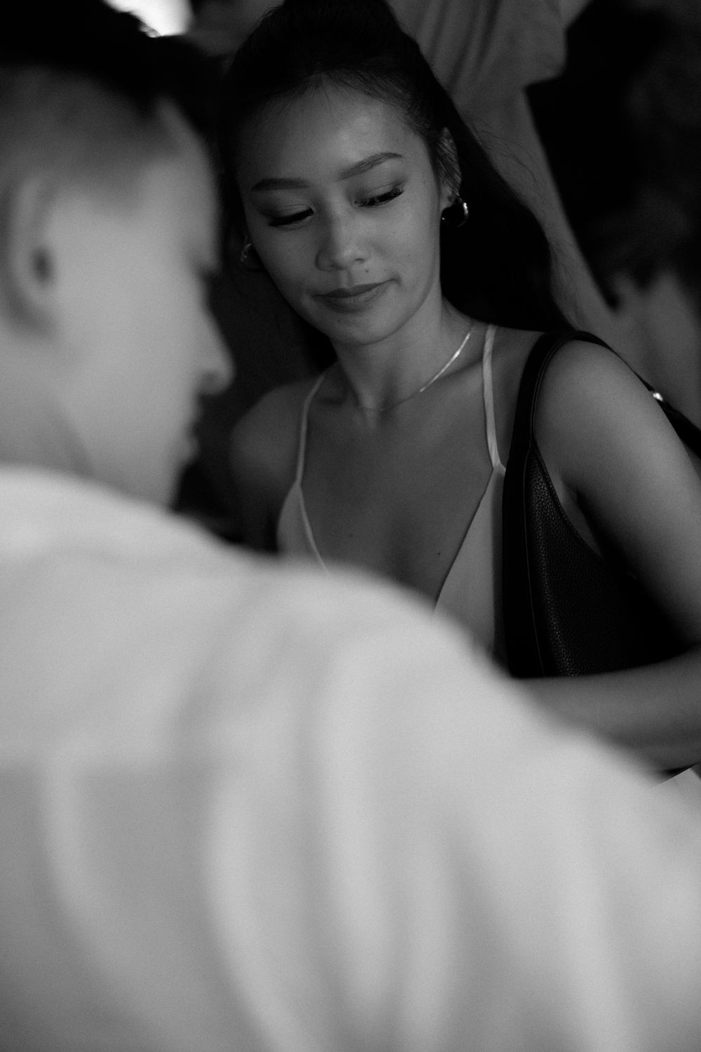 A young woman in a black dress looks down thoughtfully in a black and white close-up portrait.