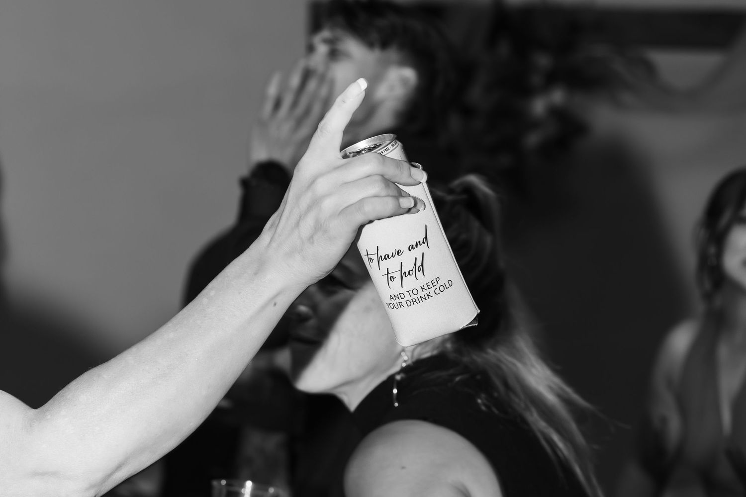 A black and white photo shows a raised hand holding a drink can during what appears to be a party or gathering.