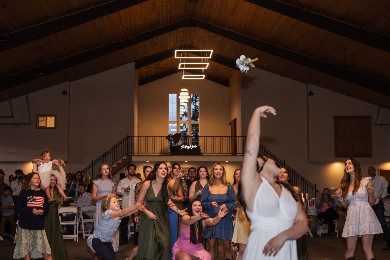Wedding guests dancing and celebrating on a dance floor inside a rustic venue with wooden beams and warm lighting.