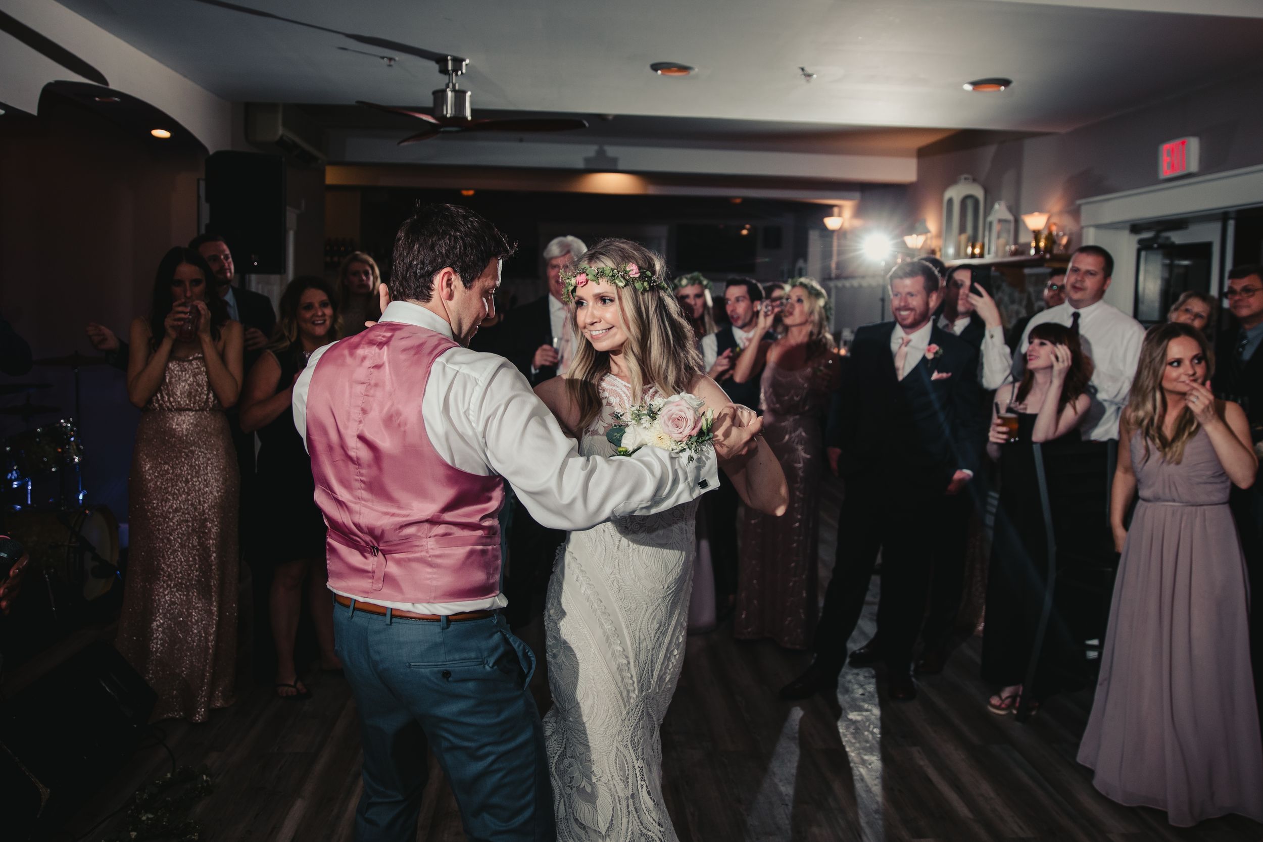 Bride and groom share first dance surrounded by cheering wedding guests at a romantic indoor reception.